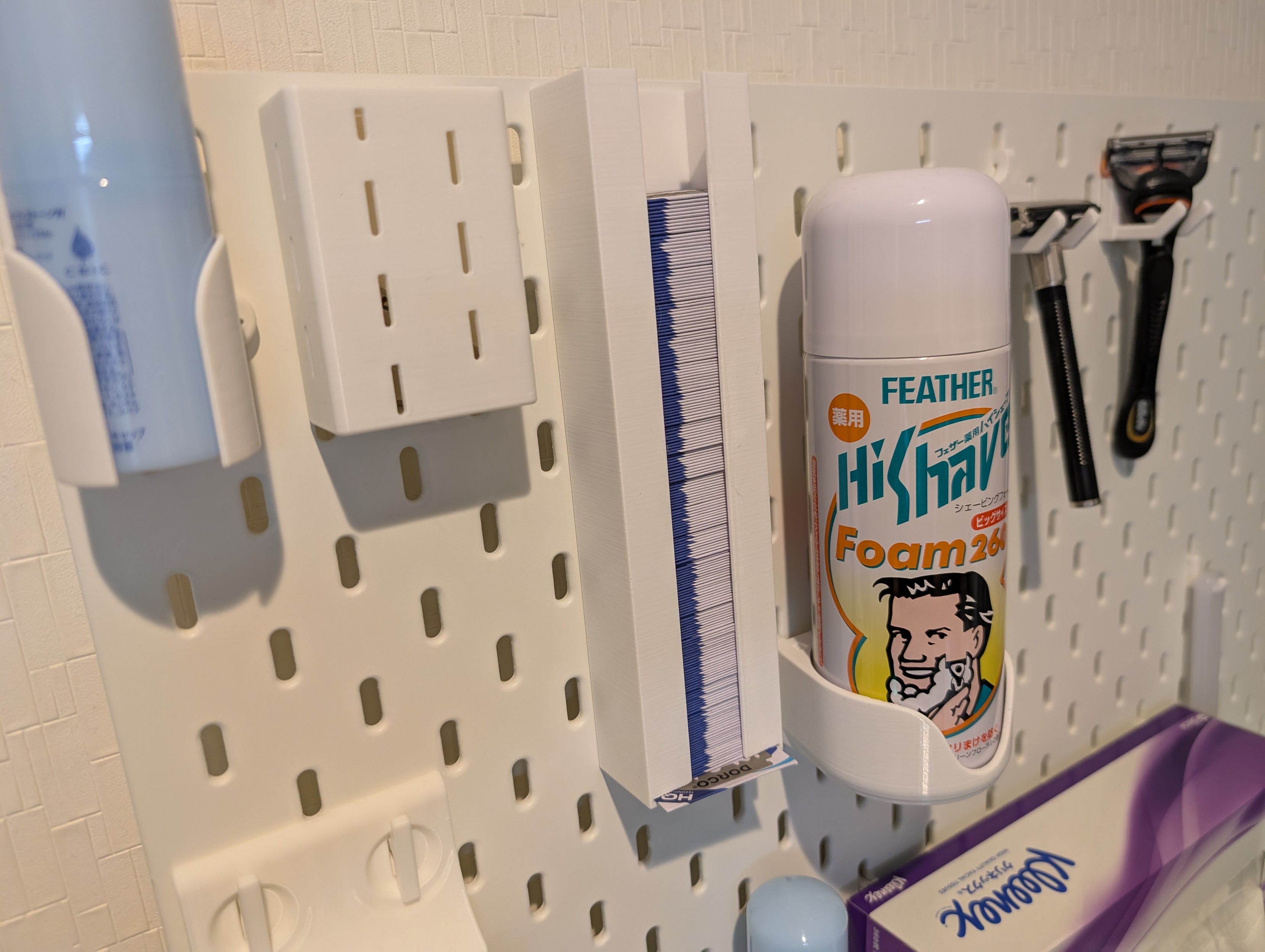 An Ikea SKADIS pegboard with 3d printed washroom accessories for holding shaving supplies and whatnot.  In the center is a safety blade dispenser, stocked with over 200 safety blades.