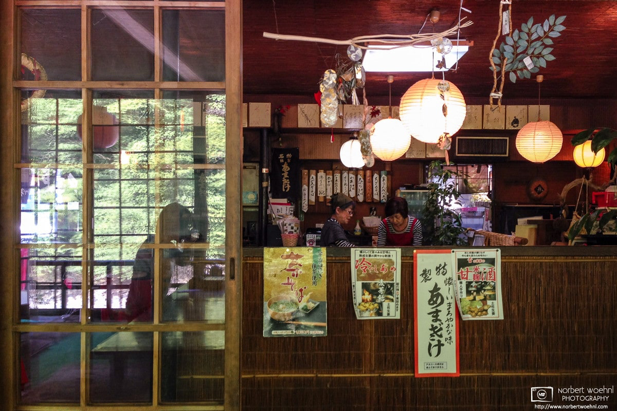 At a noodle restaurant in Takao north of Kyoto, Japan, an interior reflection from a glass door is seen together with the proprietors who are working behind a counter.